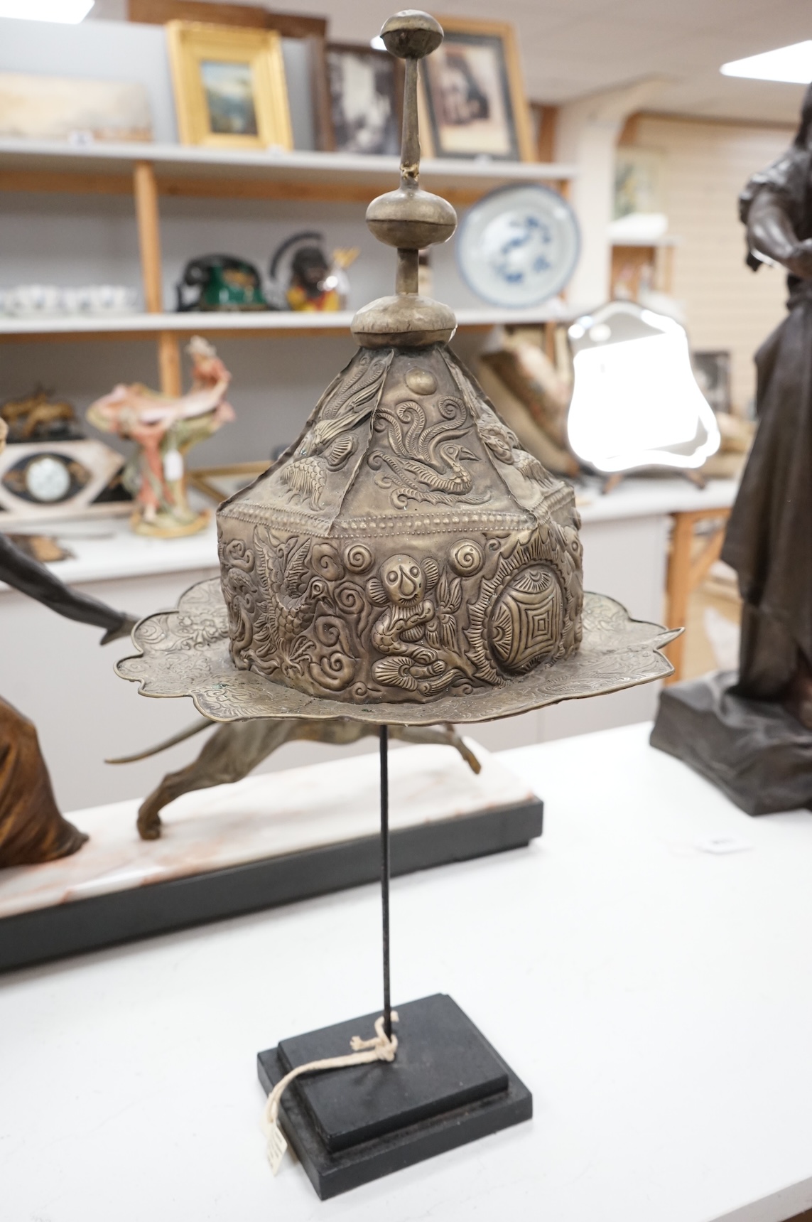 A Chinese Miao tribe embossed metal ceremonial headdress on stand, 63cm high